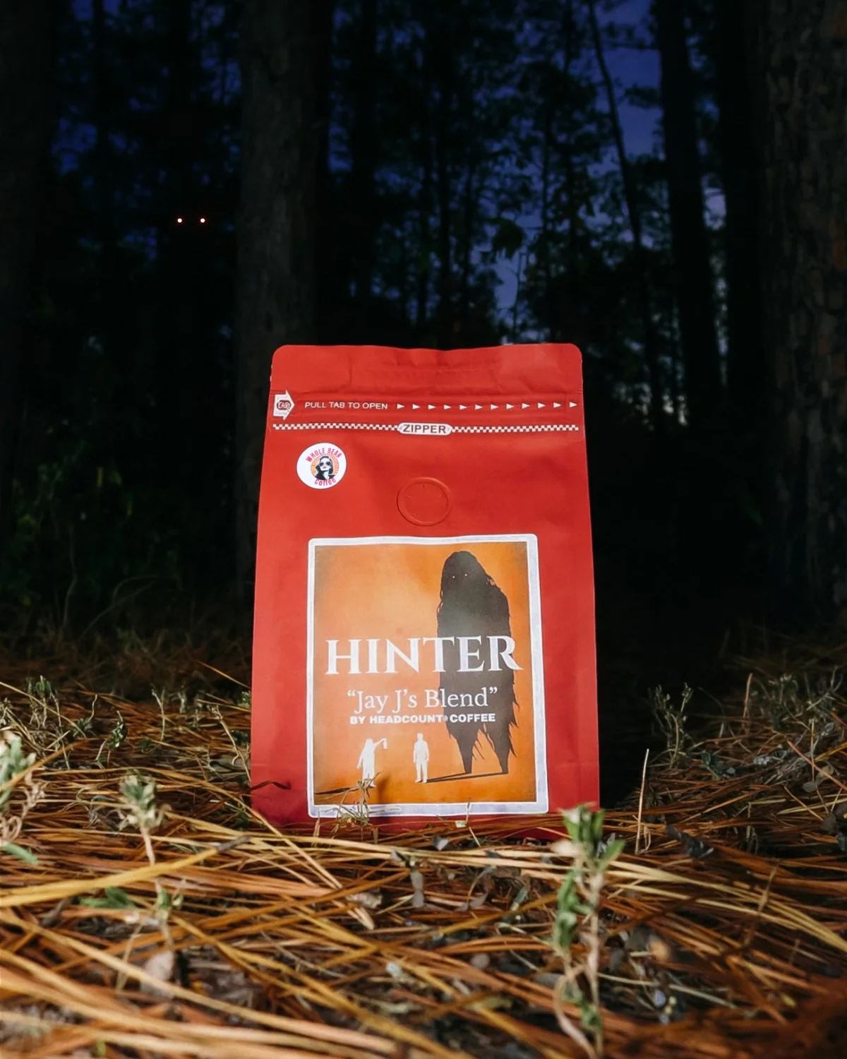 Jay J’s Blend in a red Hinter-branded bag, resting on pine needles in a dark forest